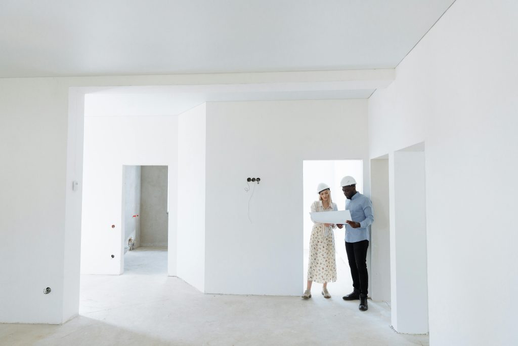 Two architects discuss building plans in a bright, unfinished room.