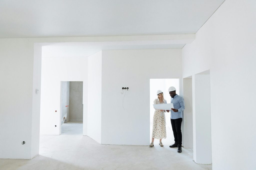 Two architects discuss building plans in a bright, unfinished room.